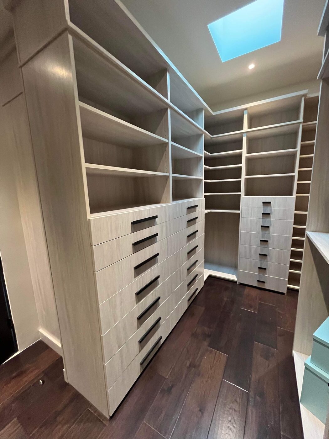 Walk-in closet under a skylight with drawer banks and adjustable shelving — Luxe Carpentry Group, San Diego