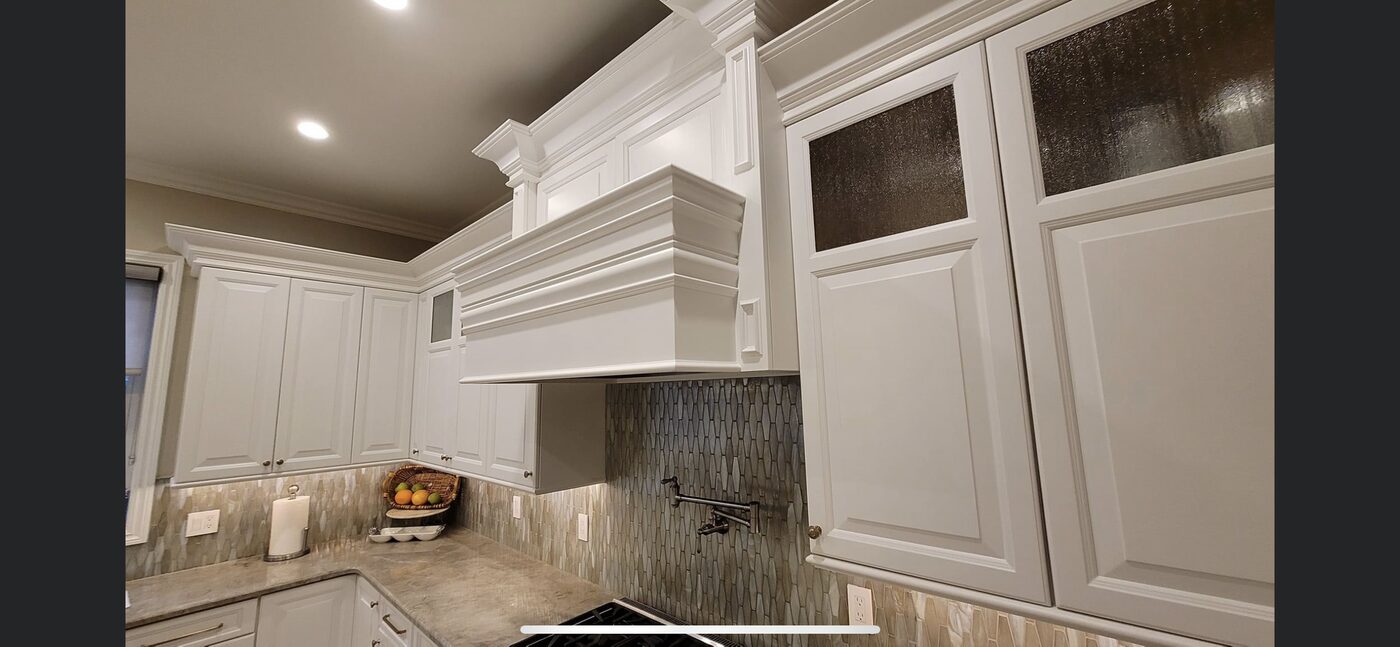 Painted range hood surround with crown moulding and glass-front upper cabinets — Luxe Carpentry Group, San Diego